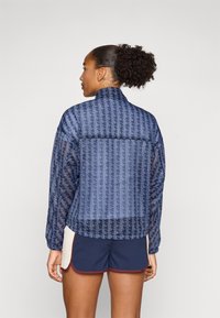 Navy patterned windbreaker jacket with a high collar, elasticated cuffs, and a transparent texture featuring geometric designs.