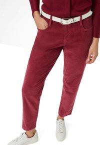 Pantaloni in corduroy rossi con design a gamba dritta, dotati di tasca frontale e cintura bianca. Abbinati a sneaker bianche per un contrasto.