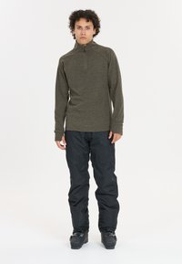 Olivengrøn, langærmet zippertrøje med høj krave parret med sorte, vandtætte bukser. Outfittet er praktisk til udendørs aktiviteter.