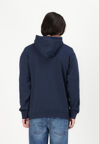Sweatshirt à capuche bleu marine avec manches longues, ourlet et poignets côtelés, fabriqué en tissu doux. La vue arrière présente un design simple et épuré sans embellissements.