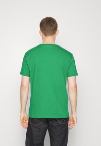 Zelené bavlněné tričko s kulatým výstřihem a krátkými rukávy, pohled zezadu. Jednoduchý design, nezdobené vzory ani akcenty.