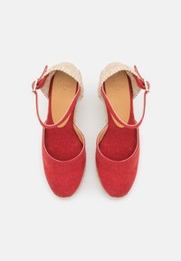 Červené plátěné espadrilky s texturovaným podpatkem z přírodního vlákna, páskem kolem kotníku a zaobleným tvarem špičky. Vnitřní podešev má hnědé kožené provedení.