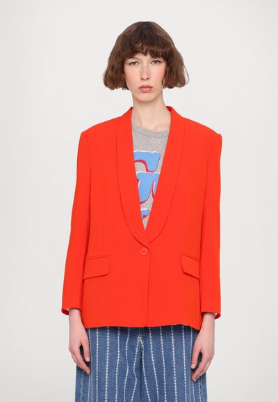 Blazer roșu aprins cu guler tip notch, două buzunare frontale și închidere cu un singur nasture, purtat peste un tricou grafic gri și pantaloni din denim cu dungi.