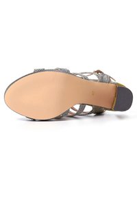 Sandalo con punta aperta, superiore in tessuto grigio e metallico, suola beige e tacco texturizzato. Presenta un design incrociato e cinturini regolabili.