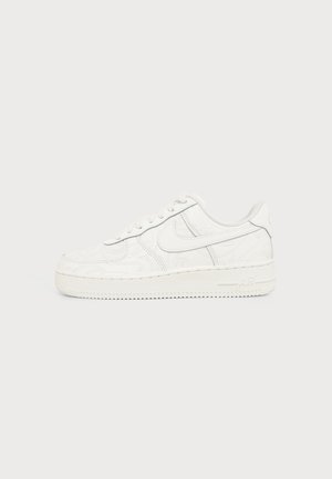 Witte Nike Air Force 1 sneaker met ingeprente draaiende patronen en een swoosh-logo aan de zijkant, tegen een effen lichte achtergrond.
