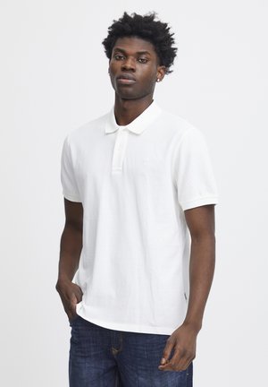 Hvid polo skjorte lavet af bomuld, med krave og korte ærmer. Subtil branding på brystet og parret med blå denim jeans.