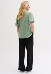 Green short-sleeve blouse with a rounded hem, paired with high-waisted black trousers. Smooth texture, casual fit, and minimalistic design.