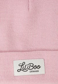 Gros plan sur un tissu tricoté rose avec une étiquette rectangulaire blanche portant du texte en cursive et en caractères d'imprimerie noirs "Lil' Boo Copenhagen."