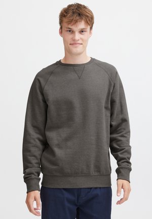 Felpa grigio scuro con scollo rotondo, maniche raglan e orlo a costine. Realizzata in materiale morbido e testurizzato. Indossata sopra pantaloni blu navy.