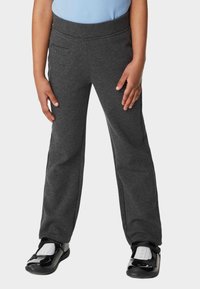 Pantalones de chándal grises con una textura suave, cinturilla elástica y bolsillos laterales, combinados con zapatos negros brillantes y calcetines blancos.