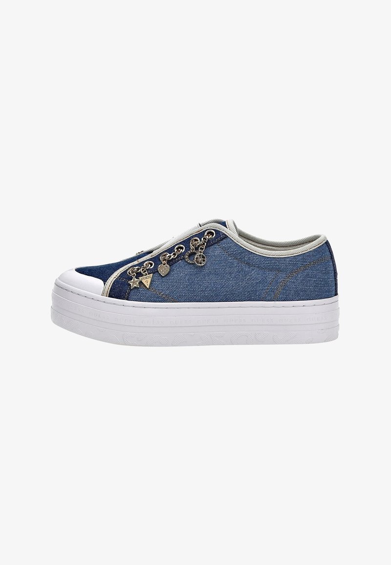 Matala denim tennarit valkoisella platolla, beige reunus ja koristeelliset metalliset riipukset sivuletsissä.