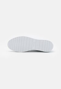 Biała podeszwa sneakerów z teksturowanej gumy, poziome rowki i branding. Gładki materiał, lekko podniesiona krawędź i minimalistyczny design.