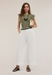 Olive green top with ruffled edges, white wide-leg trousers, black belt, black strappy sandals, and cream clutch bag with gathered detail.