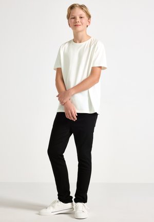 Hvid bomulds T-shirt med korteærmer, kombineret med sorte slim-fit bukser og hvide sneakers. Rent design, ingen synlige mønstre eller accenter.