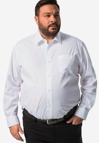 Biała, długosyowa koszula zapinana na guziki z kieszonką na piersi, z klasycznym kołnierzykiem i mankietami. Noszona z czarnymi spodniami i paskiem. Gładka tekstura.