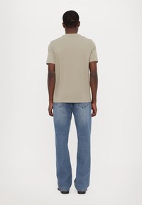 Olivengrønn kortermet t-skjorte kombinert med lyseblå denimjeans. Stoffet er glatt; jeansene har rett benpassform og baklommer.