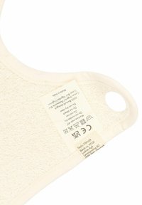 Kokvilnas samta bikses, off-white krāsā, ar apaļu formu un plānu apmali, iekļauj kopšanas etiķeti ar mazgāšanas norādījumiem.