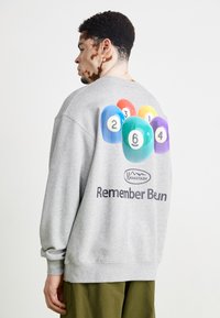 Gray sweatshirt made of soft fabric. Features colorful billiard ball graphics in varying colors and numbers on the back, with logo text below.