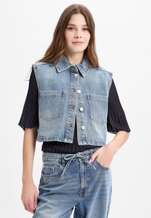 Jeansweste, hellblau, ärmellos, mit Kragen. Verfügt über zwei aufgesetzte Taschen und eine Knopfleiste. Wird über einem dunkelblauen, plissierten Oberteil getragen.