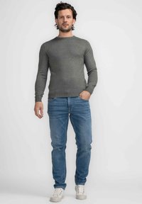 Grijze langarmtrui, slim fit, met ribbels aan de mouwen en de halslijn, gecombineerd met lichtblauwe rechte jeans en witte sneakers.