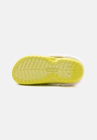 Crocs with a white fuzzy upper and a textured yellow rubber outsole, featuring a patterned tread design for grip.
