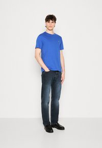 Modrý bavlněný tričko s kulatým výstřihem v kombinaci s tmavým denimem, s rovnými nohavicemi a černými botami s texturovanými detaily.