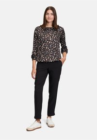 Schwarze Bluse mit Animal-Print, langen Ärmeln und Rundhalsausschnitt, kombiniert mit schwarzen Hosen und weißen Sneakers mit beigen Akzenten.