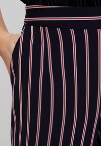 Pantalones de rayas marineras con rayas verticales en blanco y rojo, con una cinturilla plana y bolsillos laterales. La textura de la tela parece suave.