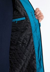 Gequilted zwarte binnenvoering met een levendige blauwe bies, voorzien van een ritszak en labels die waterdichte, winddichte en ademende eigenschappen aangeven.