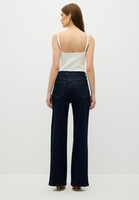 Mörkblå vida jeans med hög midja, med bakfickor och kontrasterande sömmar, kombinerat med en enkel vit spaghetti-top.