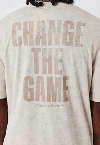 T-shirt color crema realizzato in morbido cotone con una vestibilità rilassata. Presenta una grande stampa testurizzata "CHANGE THE GAME" in beige sulla schiena.