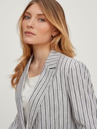 Striped blazer in white and navy with a tailored fit, featuring a notched lapel and seamless front. Worn over a white top, smooth texture.