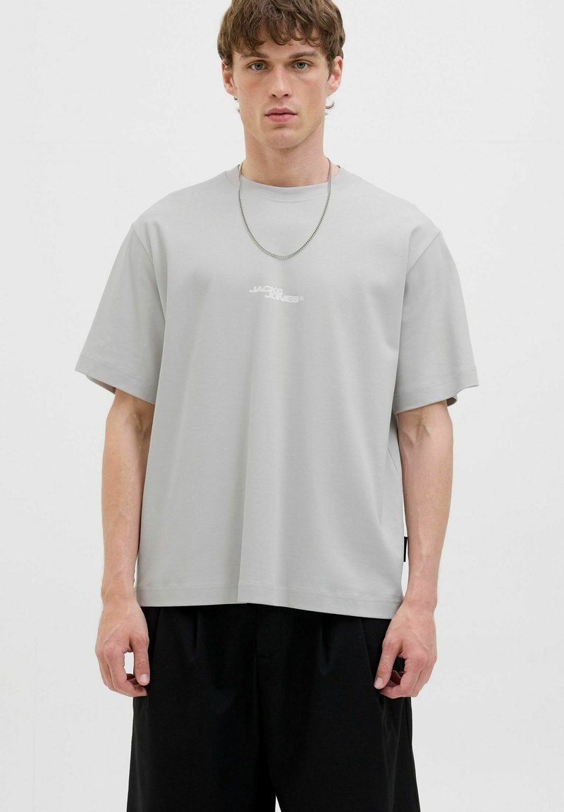 Grå bomulds T-shirt med afslappet pasform, sænkede skuldre og korte ærmer. Har et lille hvidt logo på brystet og et enkelt design.