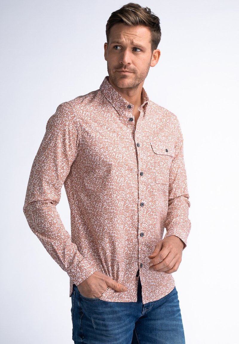 Camisa de botones de manga larga en rosa claro con patrón abstracto blanco, que incluye un bolsillo en el pecho, botones negros y un diseño ajustado.