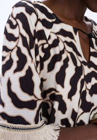 Zwart en crèmekleurig patroon top met bloemmotieven, een ronde hals, en textiel met een textuur en franjes op de mouwen.