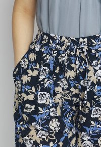 Blomstrede bukser med marineblå bund, prydet med blå og beige blomster. Lavet af et let, tekstureret stof med elastisk talje og snor.