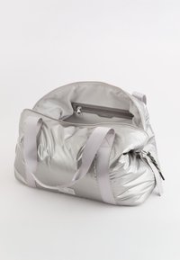 Sølvfarvet, polstret duffelbag med to grå stropper, udstyret med en lynlåslomme indeni og en farverig lynlåsgreb detalje.