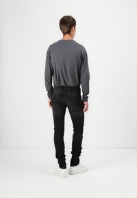 Šedá košile s dlouhým rukávem kombinována s černými džíny a bílými teniskami. Oblečení ukazuje přiléhavou siluetu a minimalistický design.