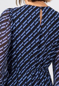 Černé šaty z látky s modrým geometrickým vzorem, s průhlednými rukávy, výstřihem ve tvaru klíče na zádech a elastickým pasem pro fitted vzhled.