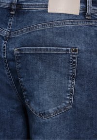 Jeans de denim con un acabado azul oscuro. Presentan un bolsillo trasero con un sencillo detalle de botón y costura en contraste. Textura suave.