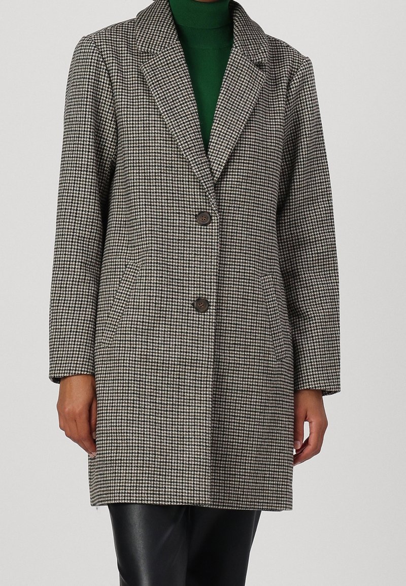 Abrigo de patrón houndstooth en gris y blanco con solapas acentuadas, dos botones, bolsillos laterales y mangas largas. Fabricado con un tejido texturizado.