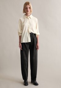 Kremfarget skjorte med krage, parret med høyt liv svarte bukser og svarte hæl boots. Enkelt design og avslappet passform.