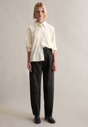 Beżowa koszula zapinana na guziki z kołnierzykiem, zestawiona z czarnymi spodniami o wysokim stanie i czarnymi botkami na obcasie. Prosty design i luźny krój.