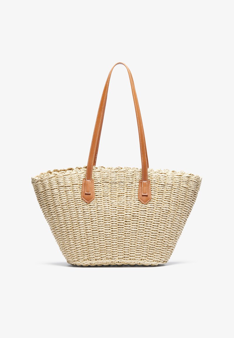 Woven straw tote bag in light beige with two brown leather handles and triangular base, featuring a textured surface and scalloped rim.