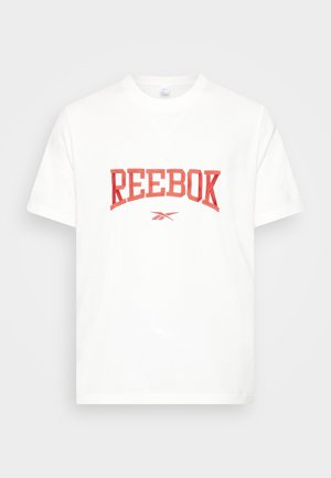 Hvid T-shirt med korte ærmer med rød "REEBOK"-tekst og logo centreret på brystet mod en ensfarvet baggrund.