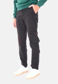 Pantaloni cargo neri con molte tasche, cuciture rosse sui ginocchi e polsini regolabili. Abbinati a sneaker bianche.