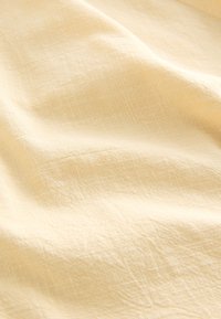 Tessuto giallo chiaro con una sottile texture e una superficie stropicciata. Presenta un delicato motivo di linee intersecting.
