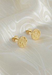 Orecchini a perno tono oro con design rotondo e lavorato. La superficie presenta una finitura scintillante e granulosa, su uno sfondo morbido e neutro.