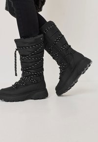 Zwarte winterlaarzen met een gepolsterde schacht, een textuurmateriaal, zwart-witte veters en een dikke, robuuste zool. Ritsdetail aan de zijkant.