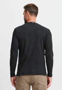 Juoda ilgo rankovėmis marškiniai, pagaminti iš lengvos medžiagos. Yra apvalios iškirptės ir subtilių siuvimo detalių. Vidutinio ilgio kirpimas su laisvu prisitaikymu.